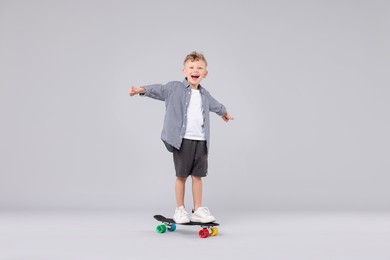 Photo of Cheerful little boy standing on penny board and showing thumbs up against gray background