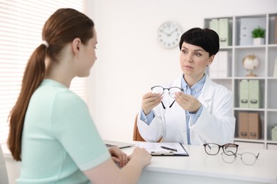 Photo of Ophthalmologist giving glasses to patient at white table in clinic