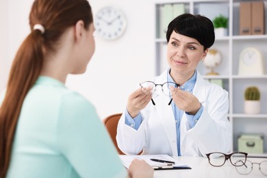 Photo of Ophthalmologist giving glasses to patient at white table in clinic