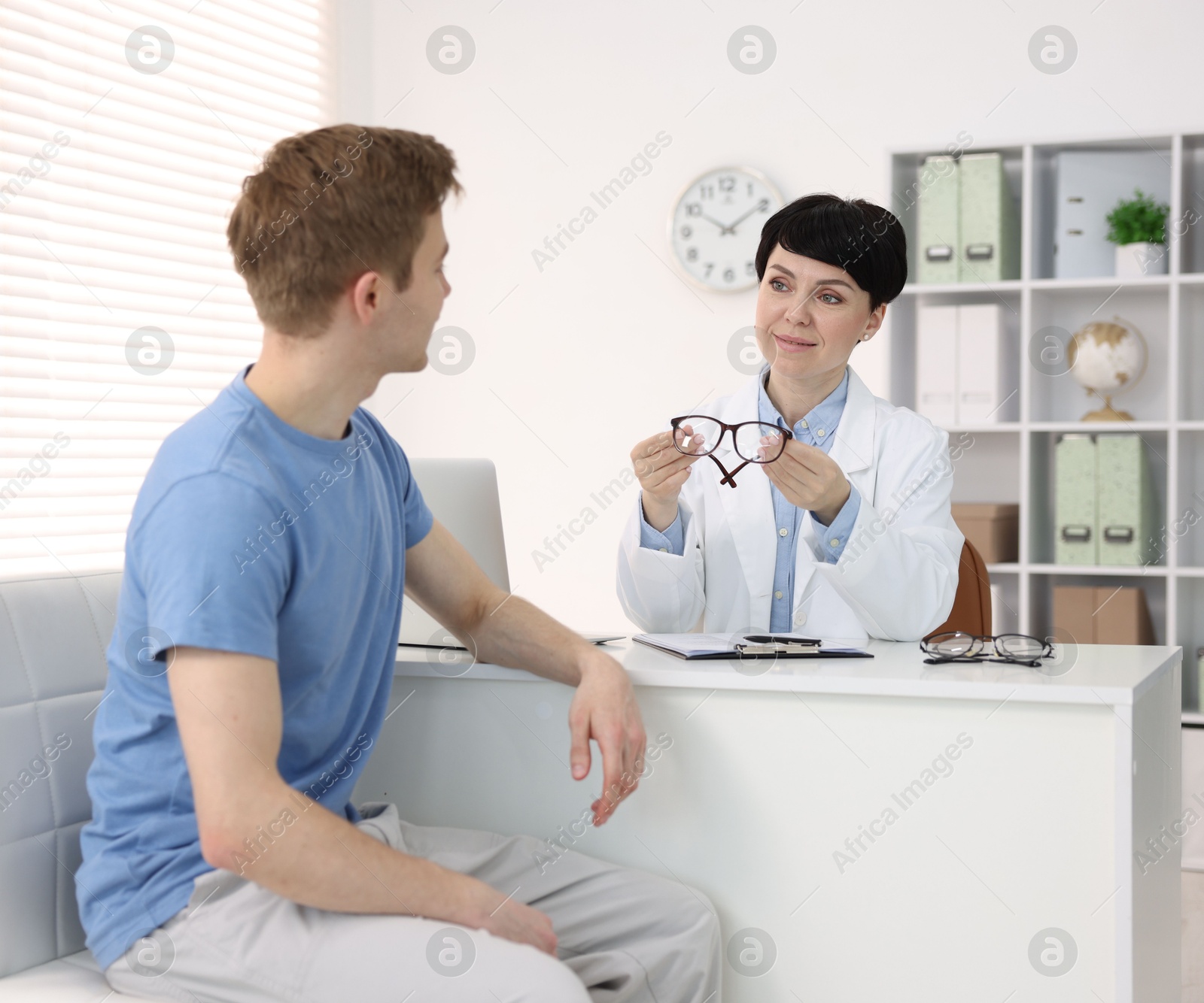 Ophthalmologist consulting young man at white table in clinic Photo of Ophthalmologist consulting young man at white table in clinic