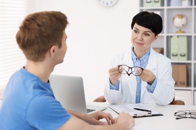Photo of Ophthalmologist consulting young man at white table in clinic