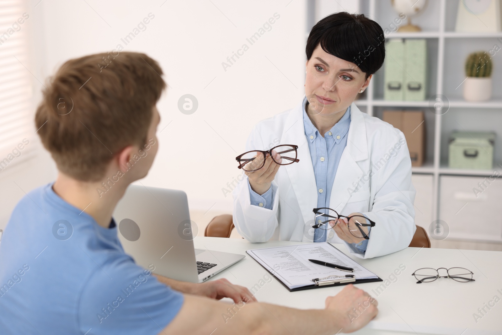 Ophthalmologist consulting young man at white table in clinic Photo of Ophthalmologist consulting young man at white table in clinic