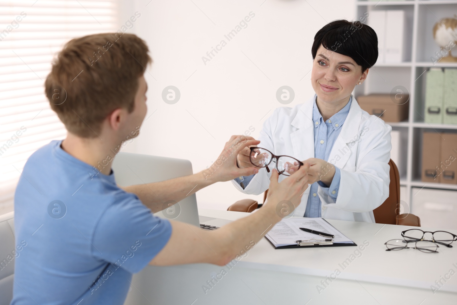 Ophthalmologist giving glasses to patient at white table in clinic Photo of Ophthalmologist giving glasses to patient at white table in clinic