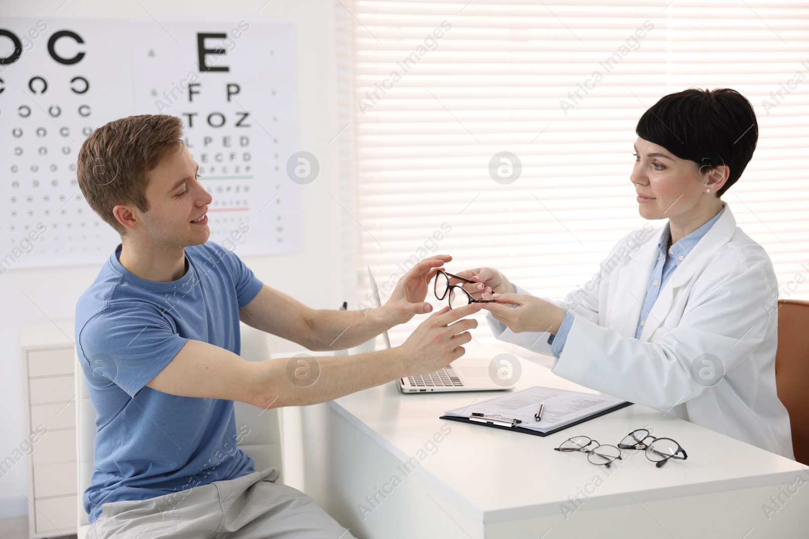 Ophthalmologist giving glasses to patient at white table in clinic Photo of Ophthalmologist giving glasses to patient at white table in clinic