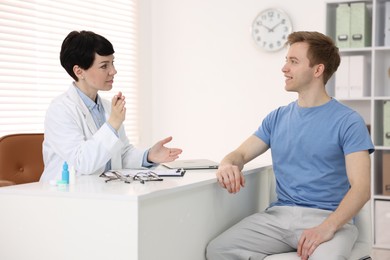 Photo of Ophthalmologist consulting young man at white table in clinic