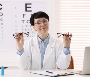 Photo of Portrait of professional ophthalmologist with glasses at white table in clinic