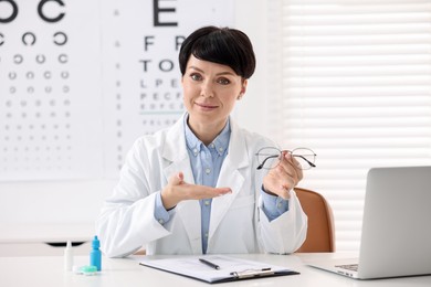 Photo of Portrait of professional ophthalmologist with glasses at white table in clinic