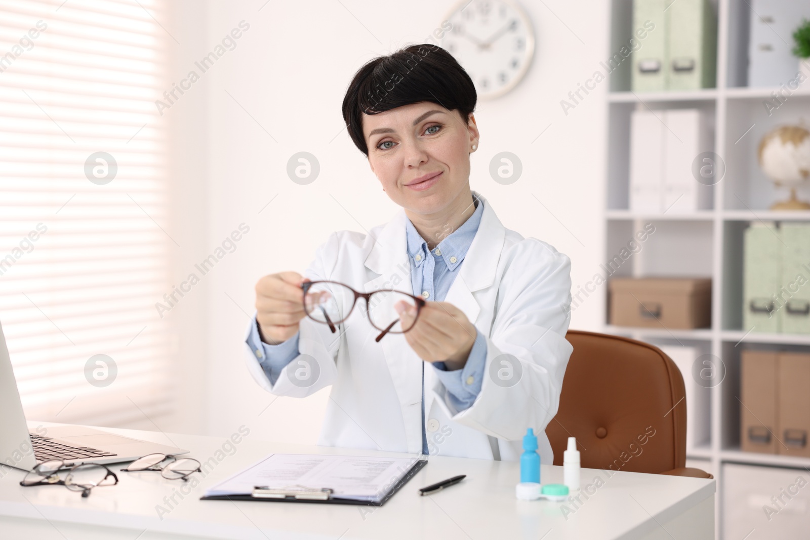 Portrait of professional ophthalmologist with glasses at white table in clinic Photo of Portrait of professional ophthalmologist with glasses at white table in clinic