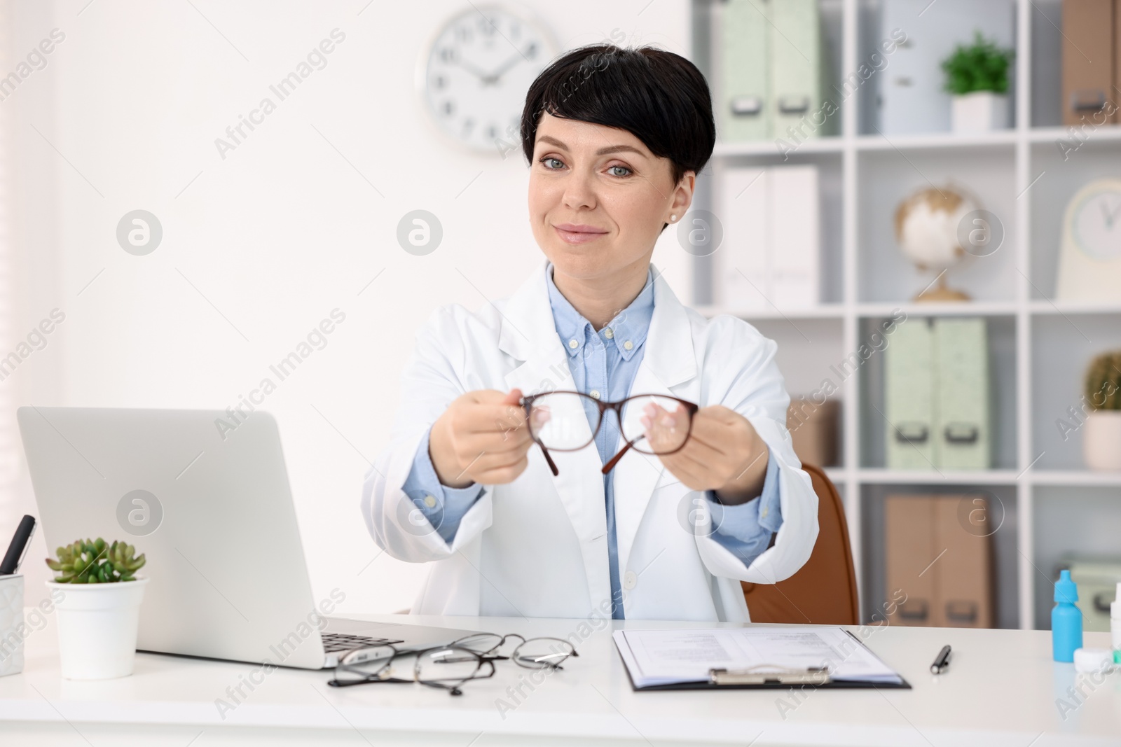 Portrait of professional ophthalmologist with glasses at white table in clinic Photo of Portrait of professional ophthalmologist with glasses at white table in clinic
