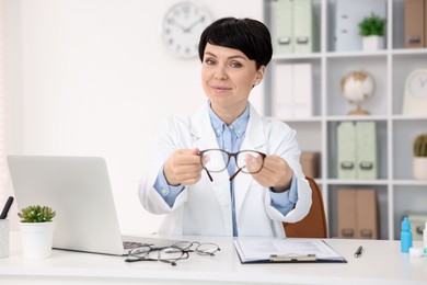 Photo of Portrait of professional ophthalmologist with glasses at white table in clinic
