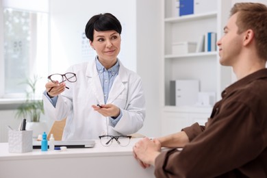 Photo of Ophthalmologist consulting young man at white table in clinic