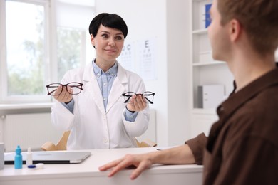 Photo of Ophthalmologist consulting young man at white table in clinic