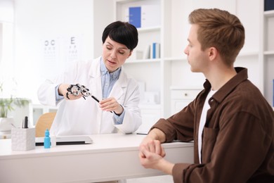 Photo of Ophthalmologist consulting young man at white table in clinic