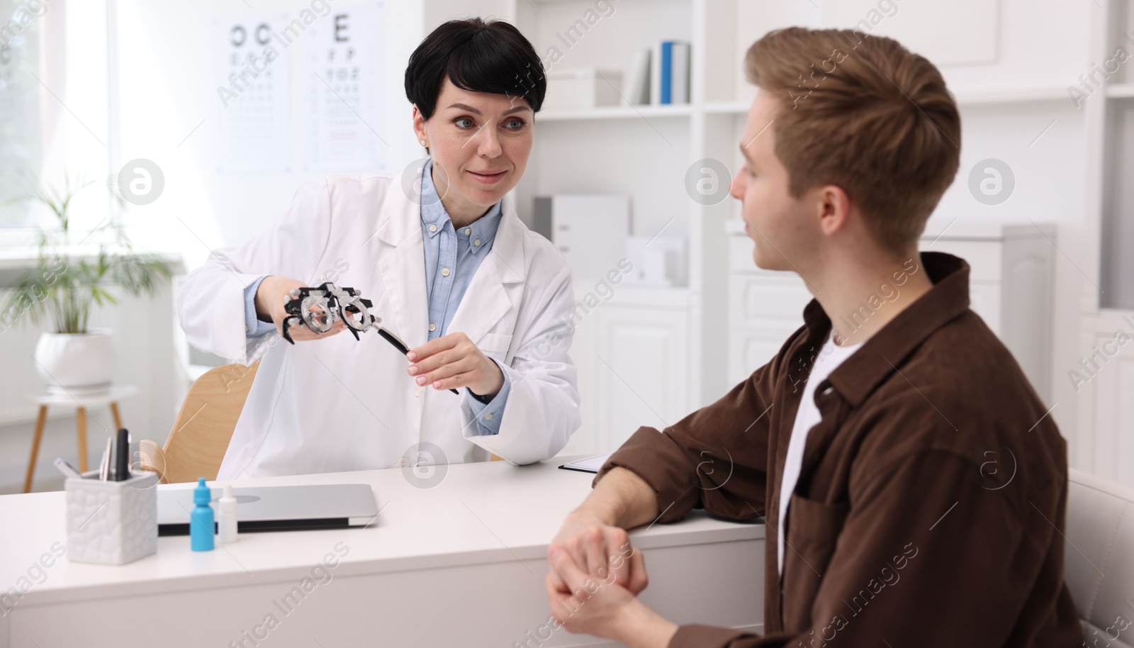 Ophthalmologist consulting young man at white table in clinic Photo of Ophthalmologist consulting young man at white table in clinic