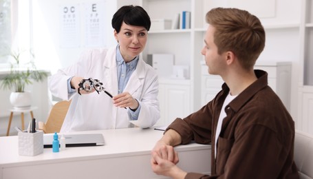 Photo of Ophthalmologist consulting young man at white table in clinic