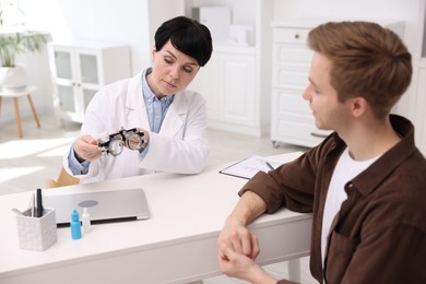 Photo of Ophthalmologist consulting young man at white table in clinic