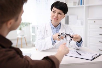 Photo of Ophthalmologist consulting young man at white table in clinic