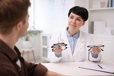 Photo of Ophthalmologist consulting young man at white table in clinic