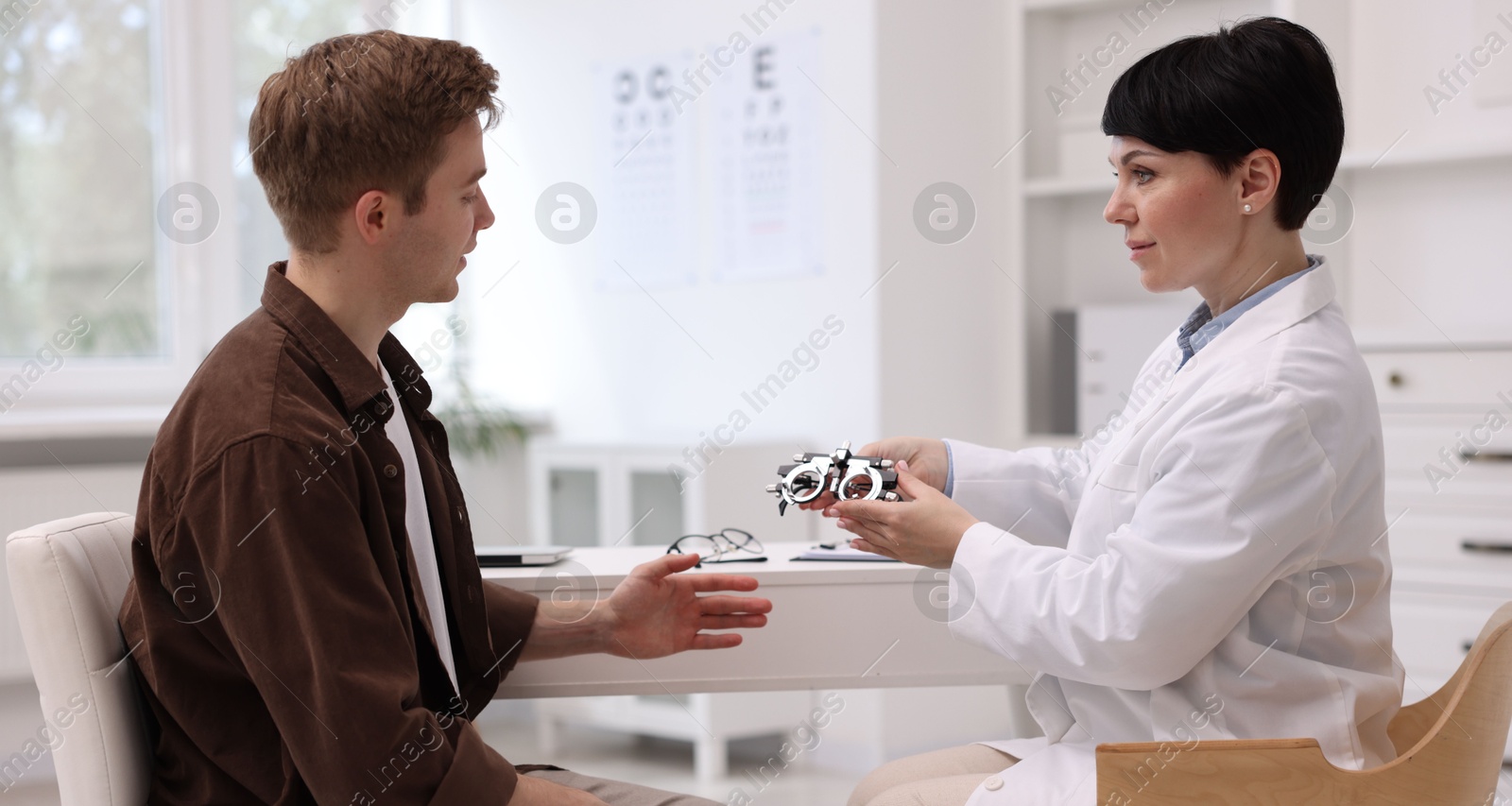 Ophthalmologist consulting young man at white table in clinic Photo of Ophthalmologist consulting young man at white table in clinic