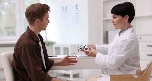 Photo of Ophthalmologist consulting young man at white table in clinic