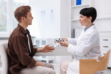 Photo of Ophthalmologist consulting young man at white table in clinic