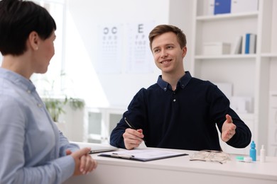 Photo of Ophthalmologist consulting woman at white table in clinic