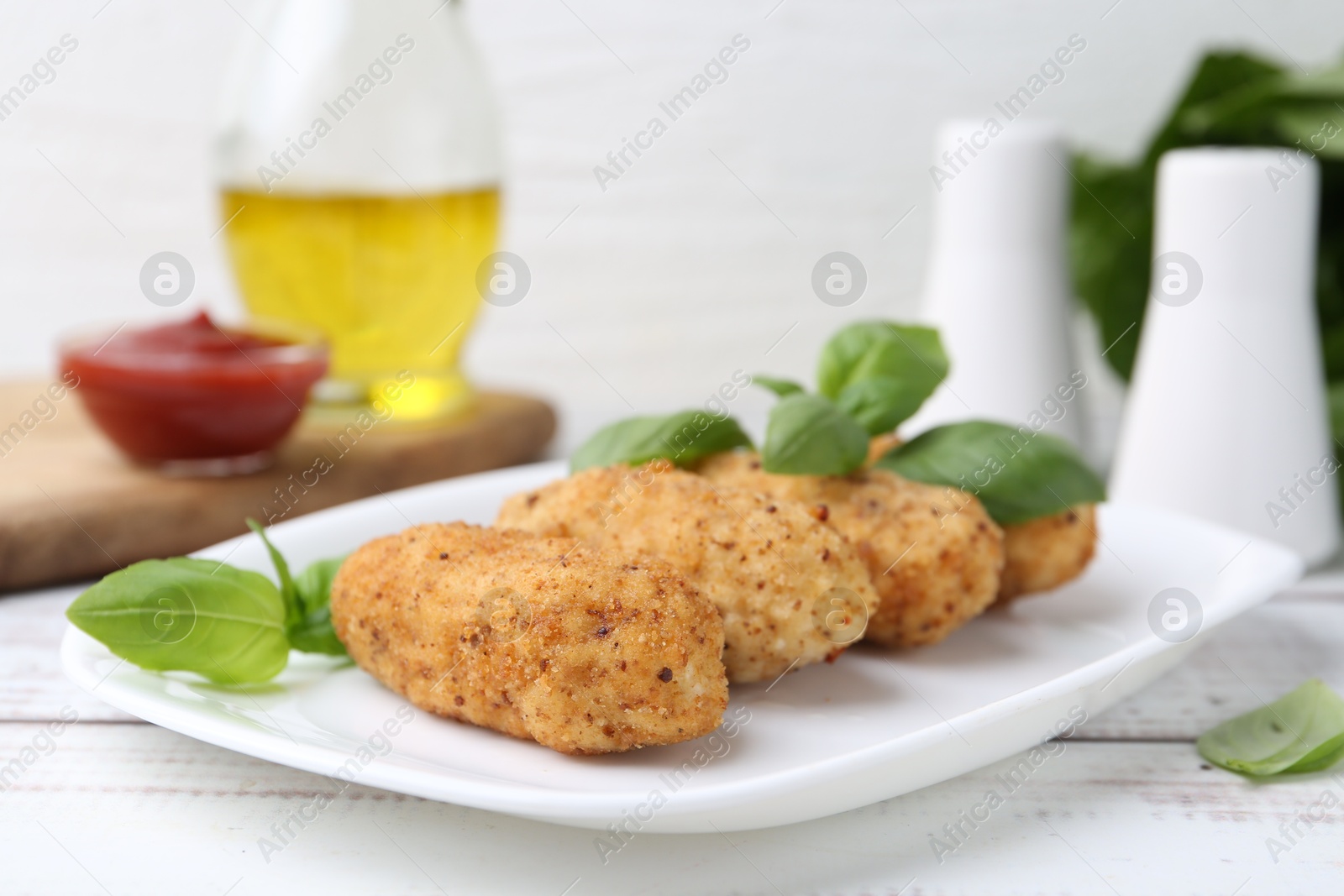 Tasty fried croquettes and basil on white wooden table, closeup Photo of Tasty fried croquettes and basil on white wooden table, closeup