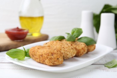 Photo of Tasty fried croquettes and basil on white wooden table, closeup