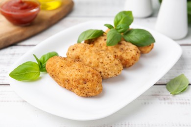 Photo of Tasty fried croquettes and basil on white wooden table, closeup