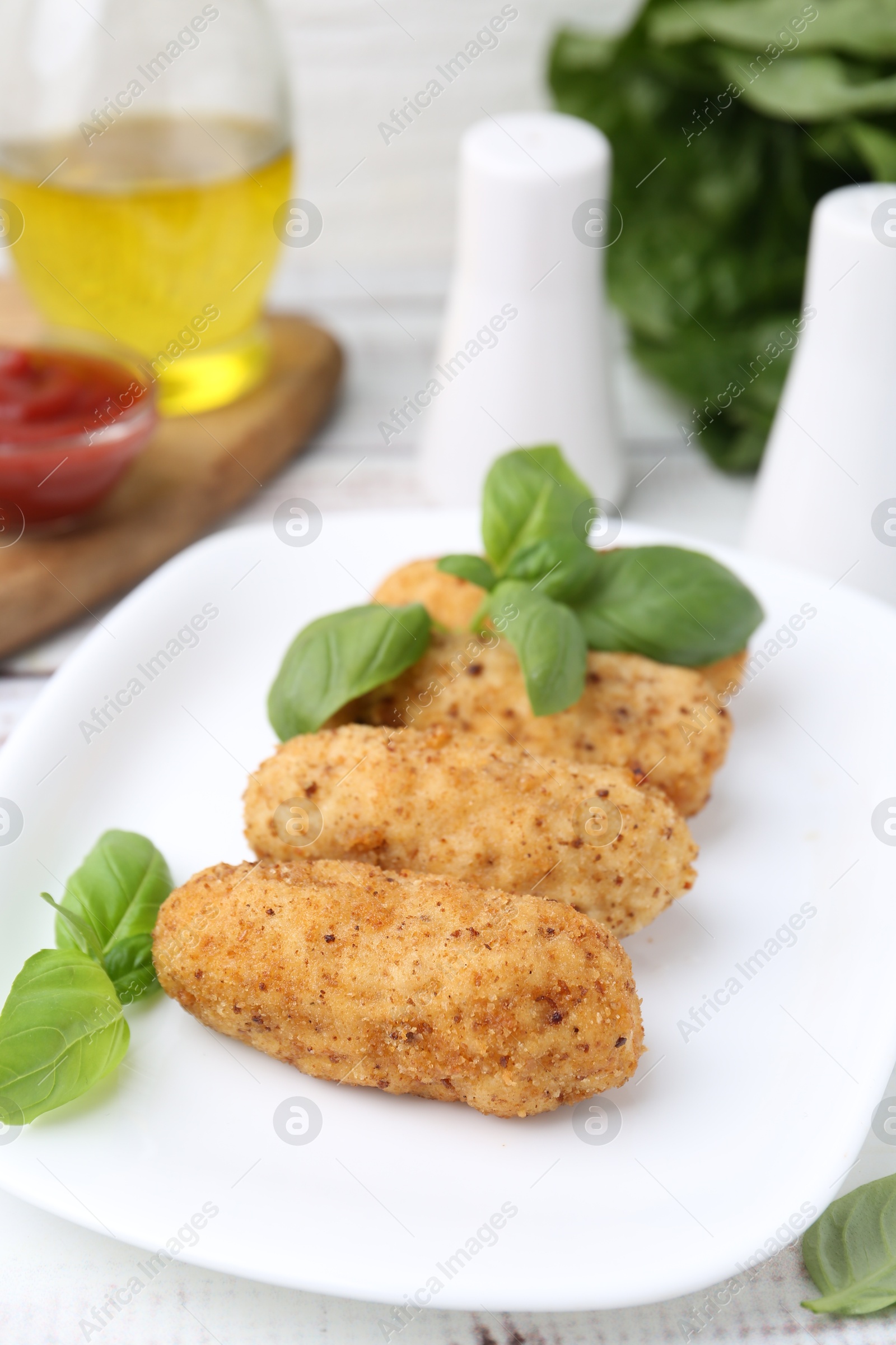 Photo of Tasty fried croquettes and basil on white wooden table, closeup