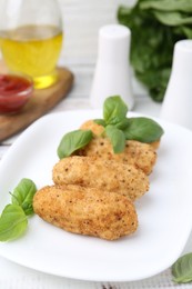 Photo of Tasty fried croquettes and basil on white wooden table, closeup