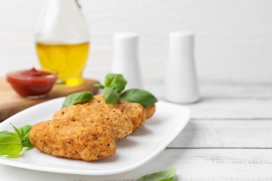 Photo of Tasty fried croquettes and basil on white wooden table, closeup. Space for text