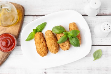 Photo of Tasty fried croquettes, basil and sauce on white wooden table, flat lay