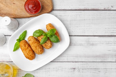 Photo of Tasty fried croquettes, basil and sauce on white wooden table, flat lay. Space for text