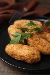 Photo of Tasty fried croquettes, parsley and sauce on wooden table, closeup
