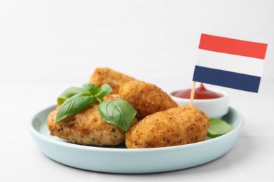 Photo of Tasty fried croquettes, basil, sauce and flag of Netherlands on white tiled table, closeup