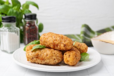 Photo of Tasty fried croquettes and basil on white tiled table, closeup