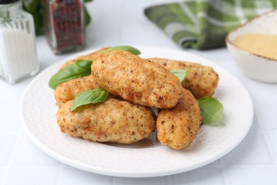Photo of Tasty fried croquettes and basil on white tiled table, closeup