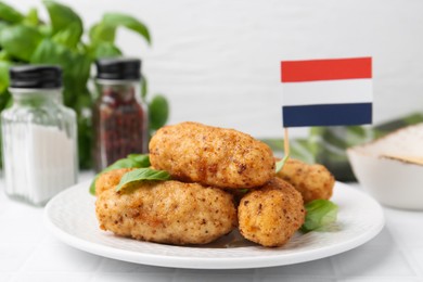 Photo of Tasty fried croquettes, basil and flag of Netherlands on white tiled table, closeup