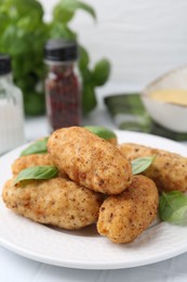 Photo of Tasty fried croquettes and basil on white tiled table, closeup