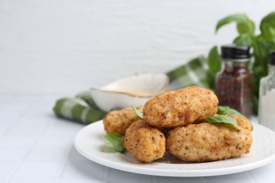 Photo of Tasty fried croquettes and basil on white tiled table, closeup. Space for text