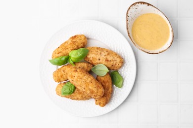 Photo of Tasty fried croquettes, basil and sauce on white tiled table, top view