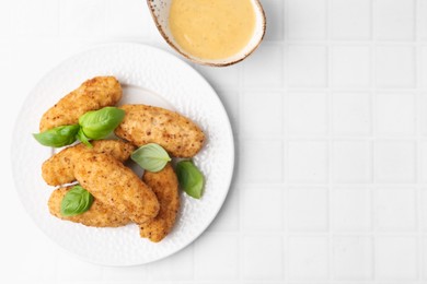 Photo of Tasty fried croquettes, basil and sauce on white tiled table, top view. Space for text