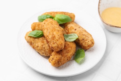 Photo of Tasty fried croquettes, basil and sauce on white tiled table, closeup