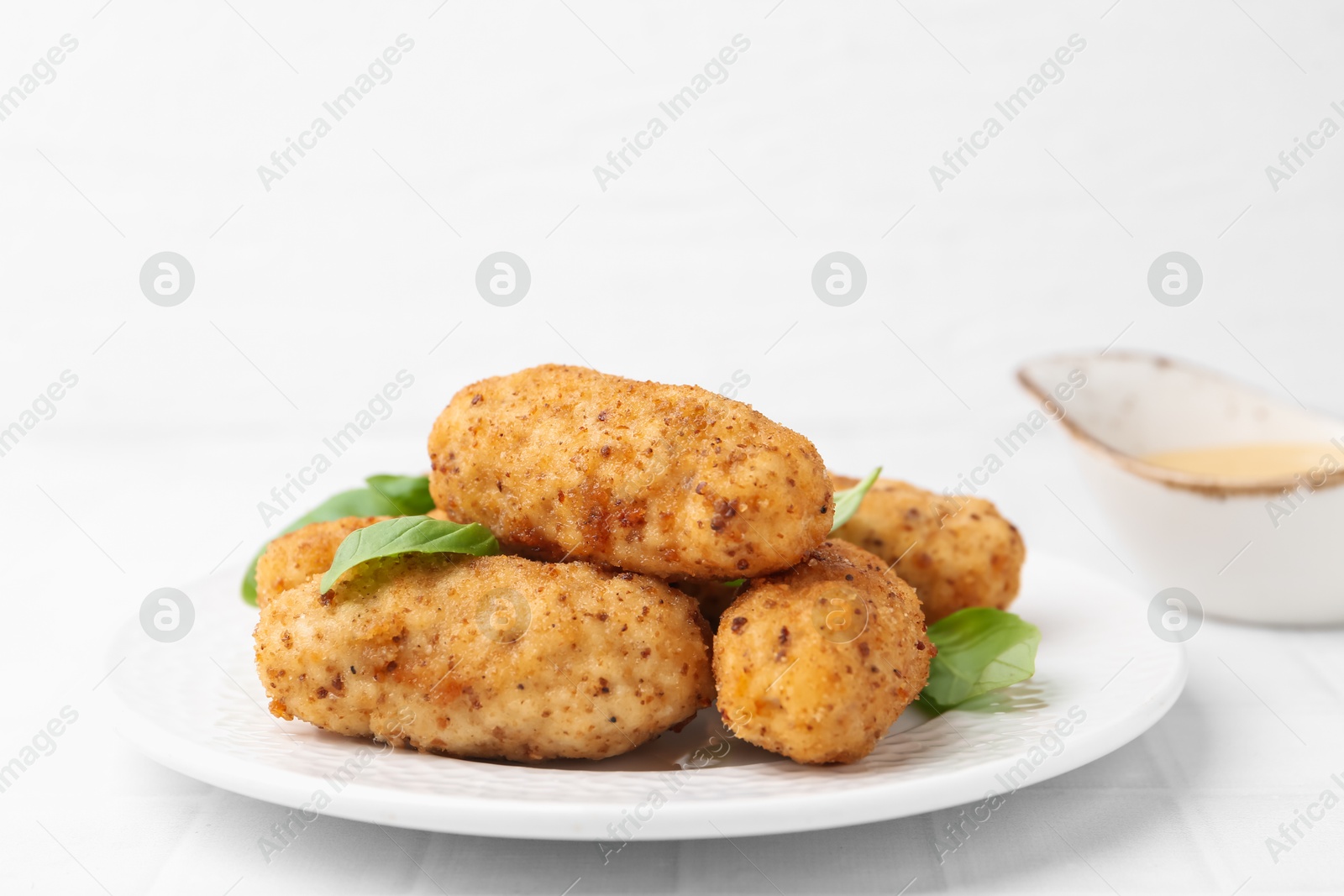 Tasty fried croquettes, basil and sauce on white tiled table, closeup Photo of Tasty fried croquettes, basil and sauce on white tiled table, closeup