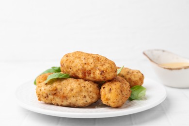 Photo of Tasty fried croquettes, basil and sauce on white tiled table, closeup