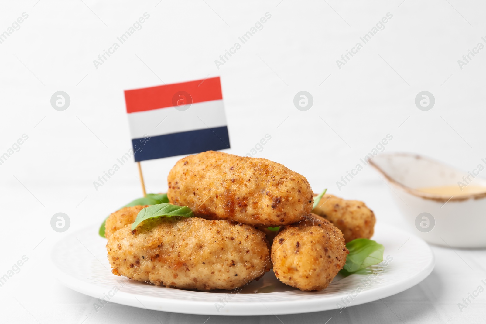 Tasty fried croquettes, basil, sauce and flag of Netherlands on white tiled table, closeup Photo of Tasty fried croquettes, basil, sauce and flag of Netherlands on white tiled table, closeup