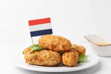 Photo of Tasty fried croquettes, basil, sauce and flag of Netherlands on white tiled table, closeup
