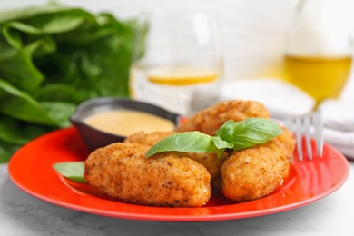 Photo of Tasty fried croquettes, basil and sauce on white marble table, closeup