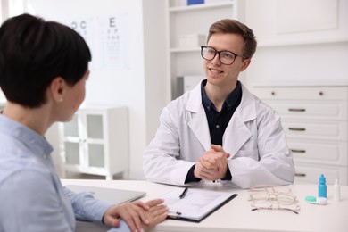 Photo of Ophthalmologist consulting woman at white table in clinic